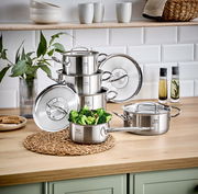 Stapel von Edelstahlkochtöpfen auf einer Küchenarbeitsplatte, mit einem Topf voller Brokkoli im Vordergrund, seitliche Perspektive.