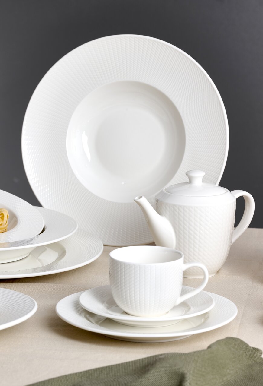 Elegantes weißes Tafelset mit feiner Struktur, bestehend aus Teller, Tasse und Kanne, aus seitlicher Perspektive fotografiert.