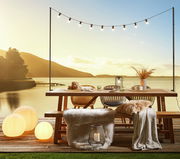 Gartentisch und Gartenbank auf einer Terrasse mit Seeblick bei Sonnenuntergang, dekoriert mit Lichtern und Kissen, seitliche Perspektive