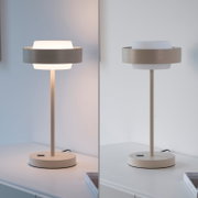 Moderne LED-Tischleuchte in Beige mit rundem Standfuß und zylindrischem Schirmring, einmal eingeschaltet und einmal ausgeschaltet, frontal in leichter Seitenperspektive auf einem weißen Sideboard