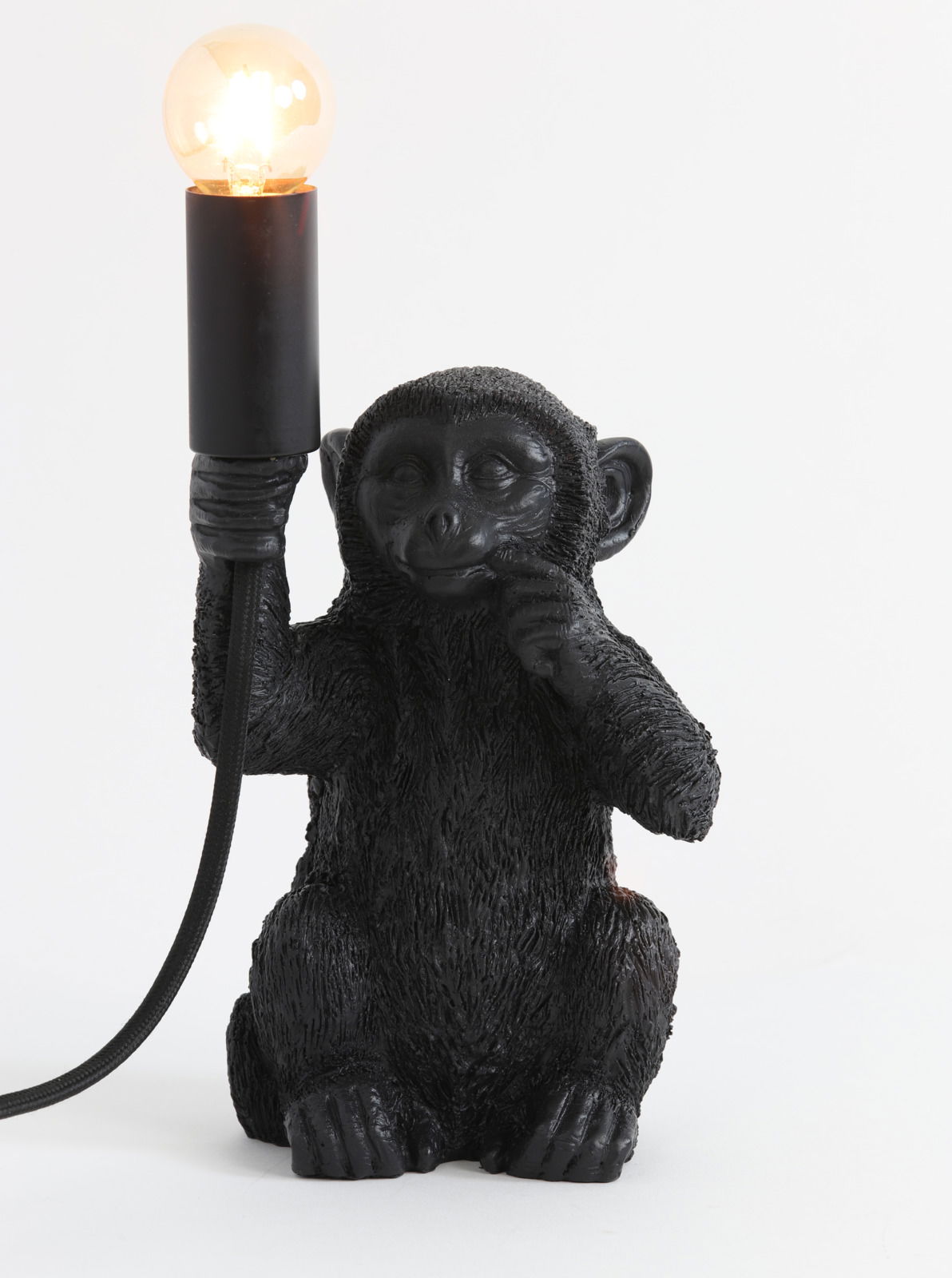 Schwarze Tischleuchte in Form eines sitzenden Affen, der eine Glühbirne in der Hand hält. Frontalansicht.