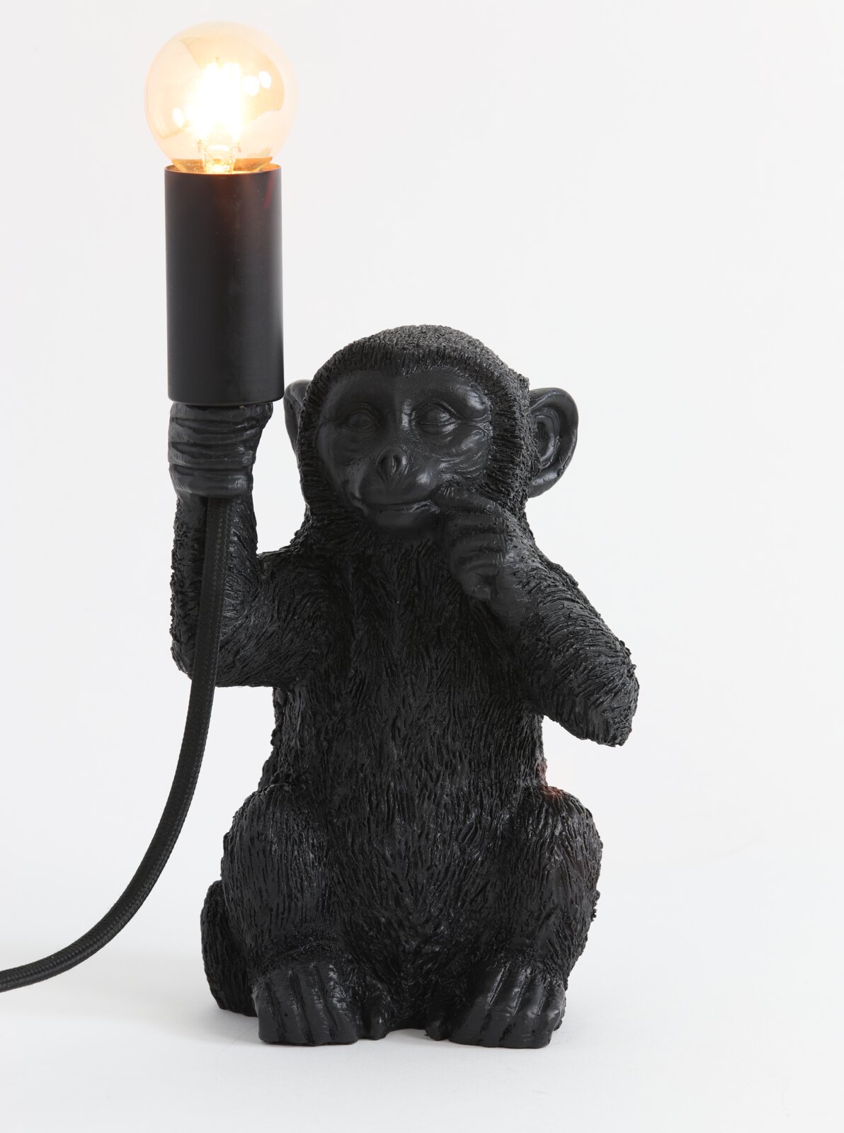 Zwarte tafellamp in de vorm van een zittende aap die een gloeilamp in zijn hand houdt. Vooraanzicht.