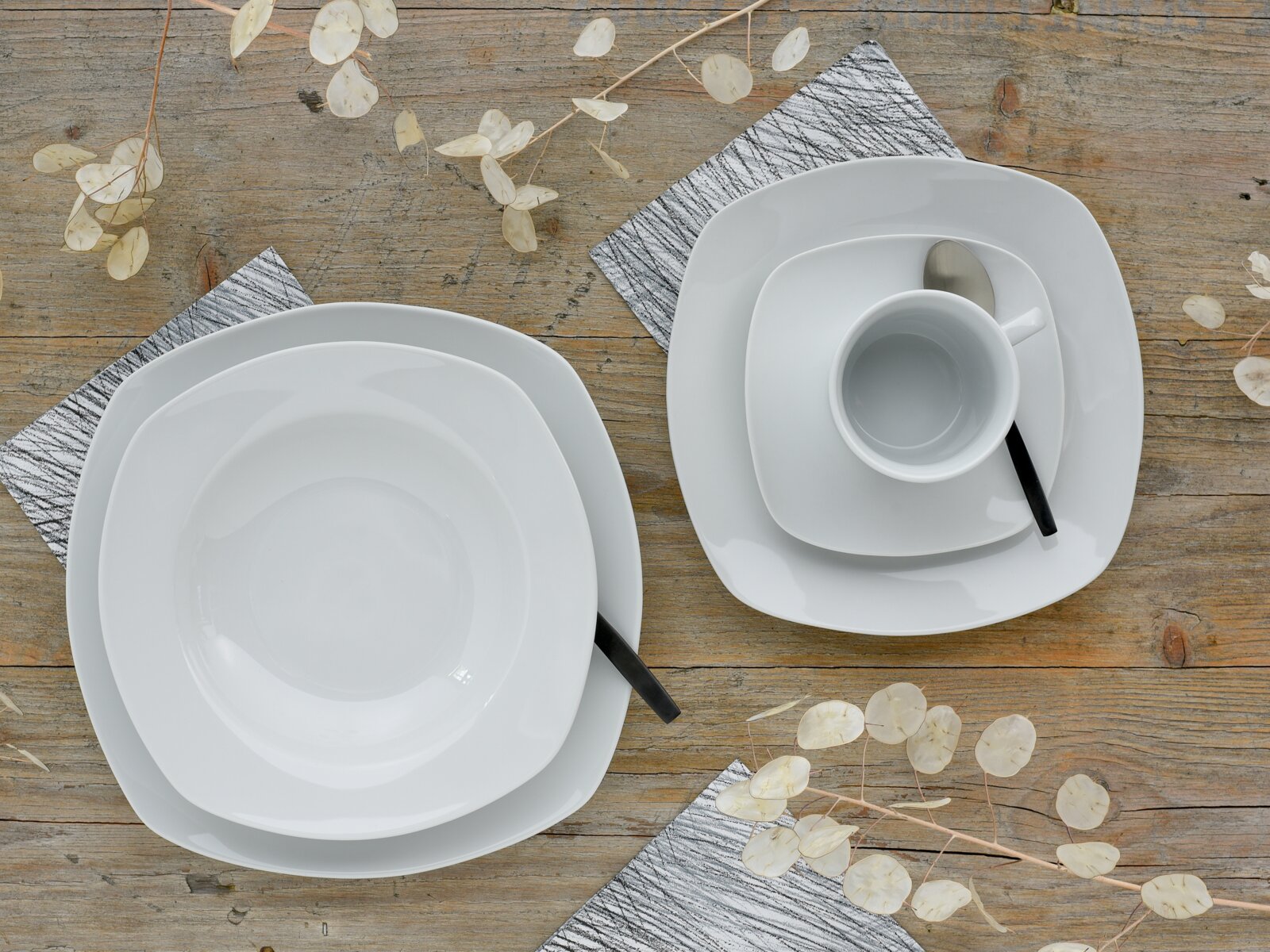 Weißes, quadratisch abgerundetes Porzellan-Geschirrset mit Teller, Schale und Tasse samt Löffel auf rustikalem Holztisch, Draufsicht von oben