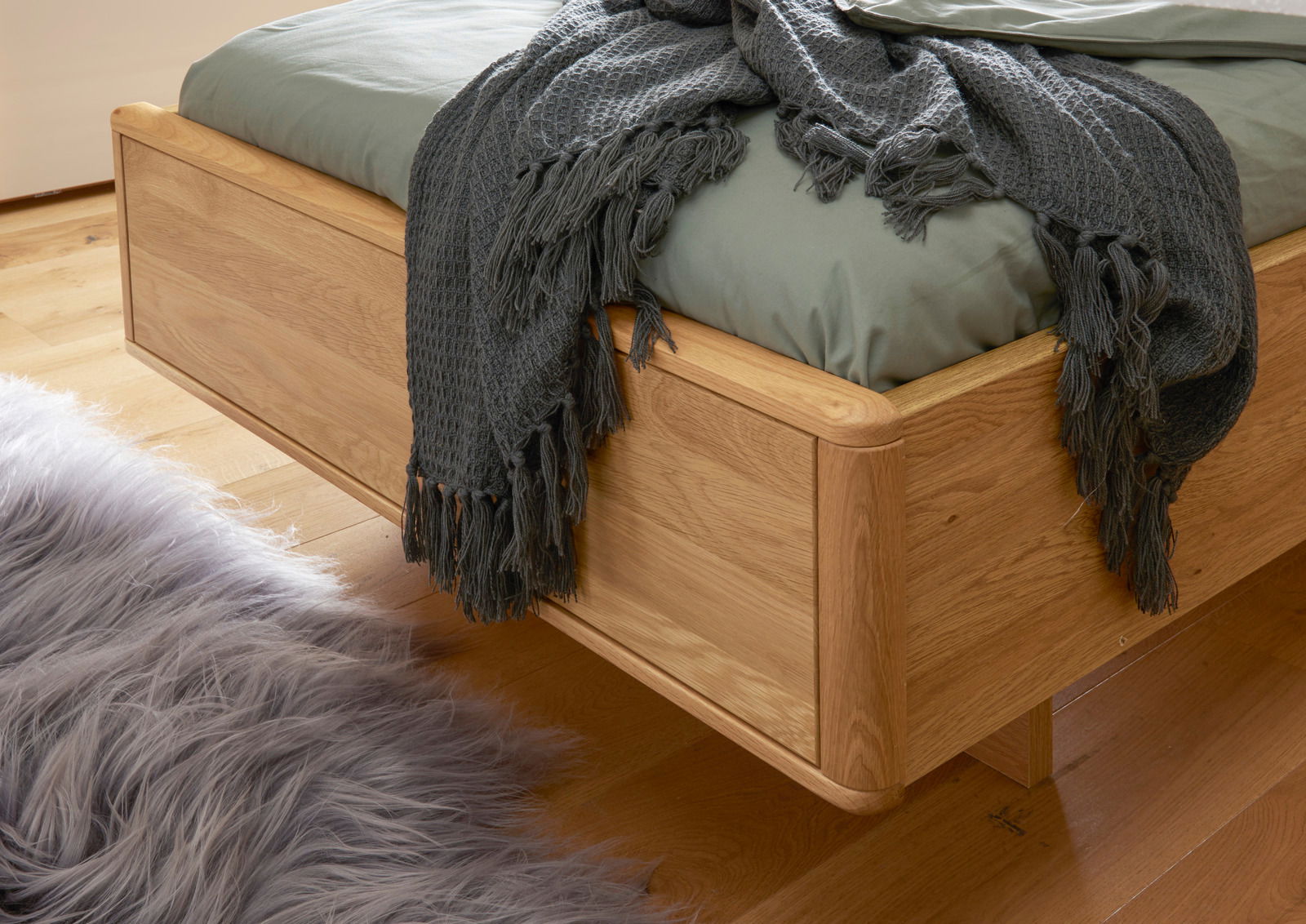 Komfortbett aus Holz mit grüner Bettwäsche und grauer Decke, seitliche Perspektive