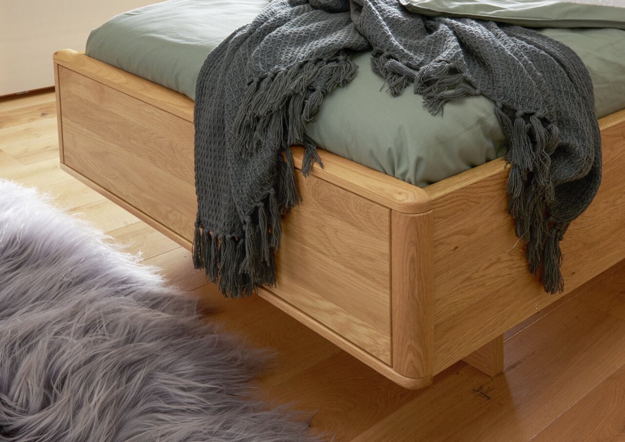 Komfortbett aus Holz mit grüner Bettwäsche und grauer Decke, seitliche Perspektive