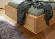 Comfortabel houten bed met groen beddengoed en een grijze deken, zijaanzicht