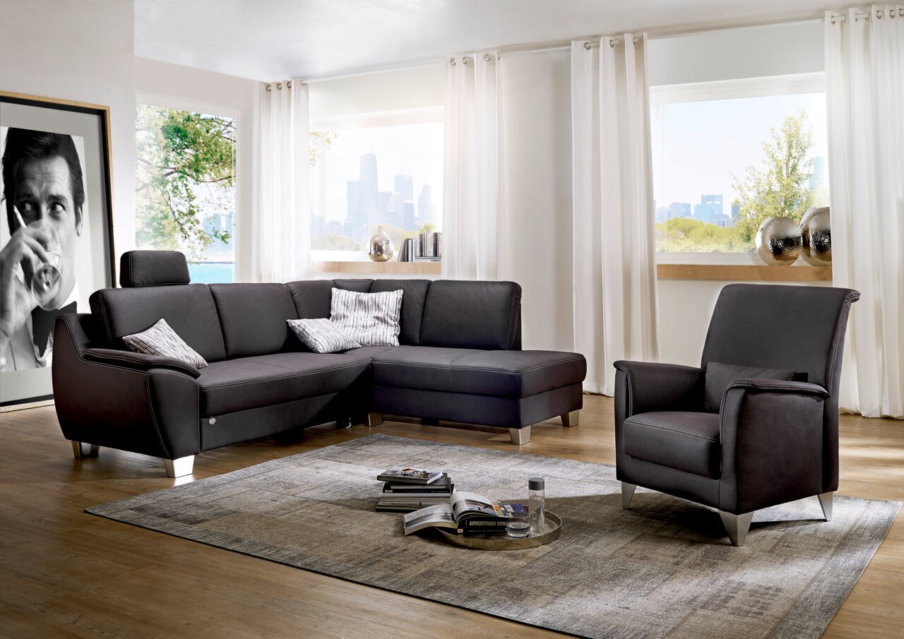 Moderne Polsterrundecke in einem hellen Wohnzimmer mit großen Fenstern, ergänzt durch einen passenden Sessel. Perspektive von vorne.