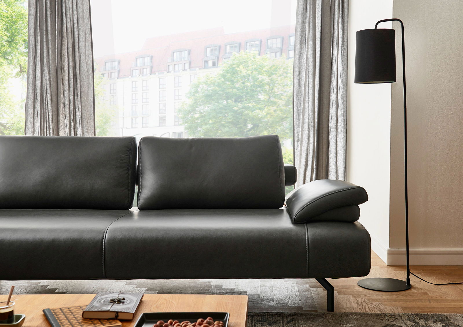 Modernes, schwarzes Ledersofa in einem hellen Wohnzimmer, seitliche Perspektive mit Blick auf die Rückenlehne und Armlehne, neben einer Stehlampe.