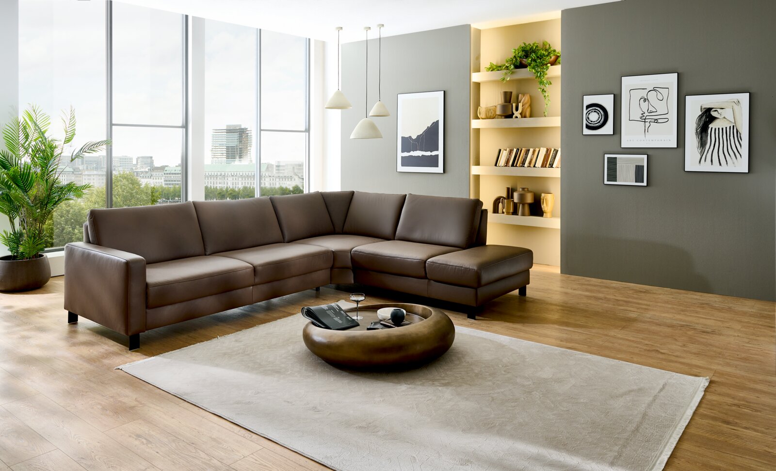 Modernes braunes Leder-Ecksofa in L-Form mit Ottomane in hellem Wohnzimmer, perspektivisch in leichter Seitenansicht von vorne fotografiert.