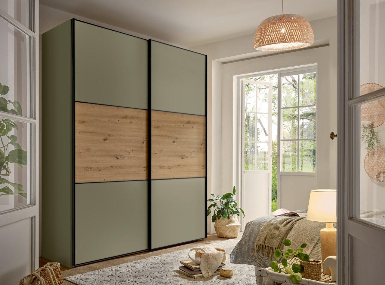 Moderne slaapkamer met grote kast met schuifdeuren in olijfgroen en houtlook, zwarte kozijnen, schuin aanzicht van linksvoor