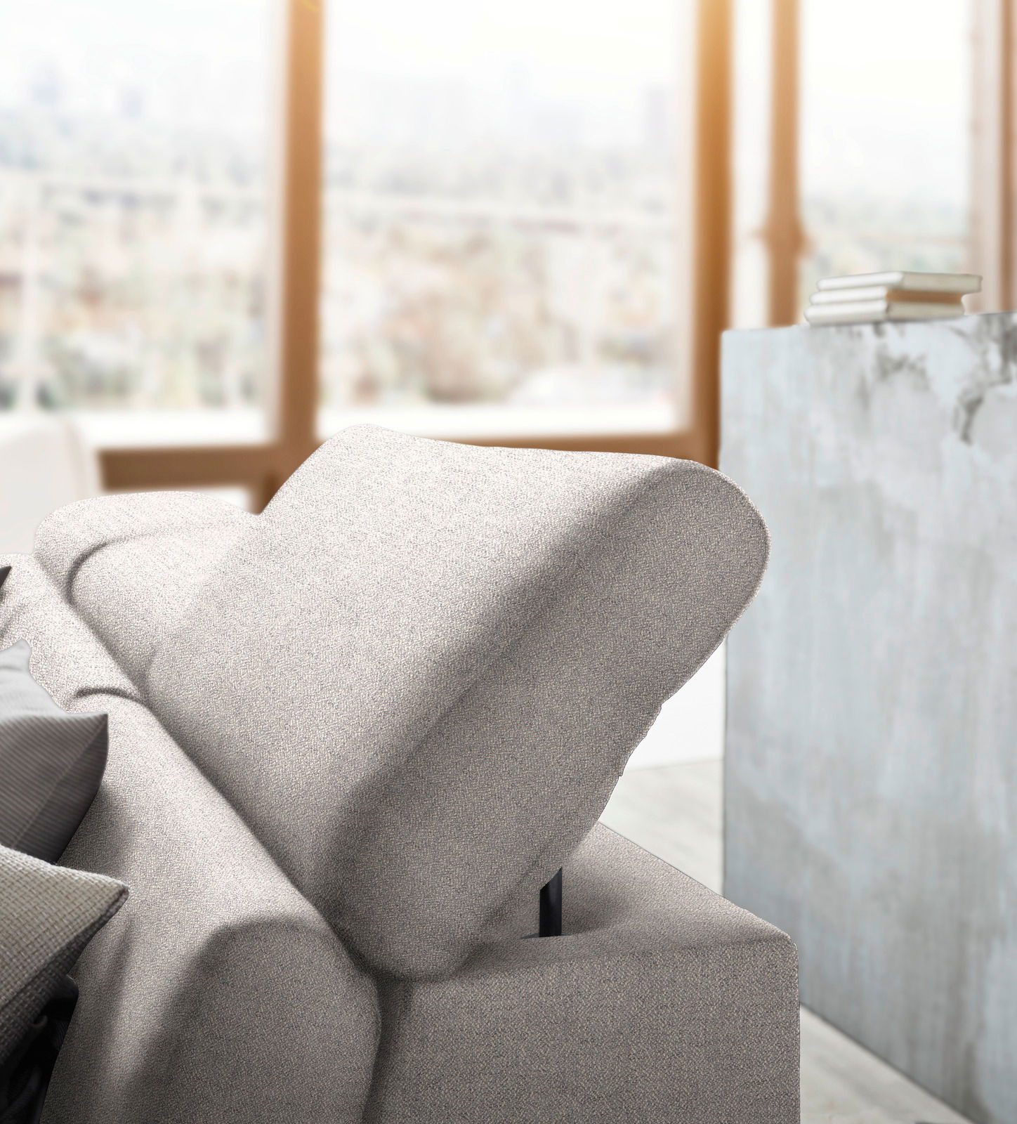 Nahaufnahme einer modernen, hellgrauen Rundecke mit verstellbarer Kopfstütze in einem hellen Raum mit großen Fenstern im Hintergrund.