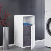 Weißer Wäschekorb-Schrank mit geöffneter Tür und grauem Stoff-Wäschesack, frontal aus leicht schräger Perspektive im modernen Badezimmer neben einer Waschmaschine.