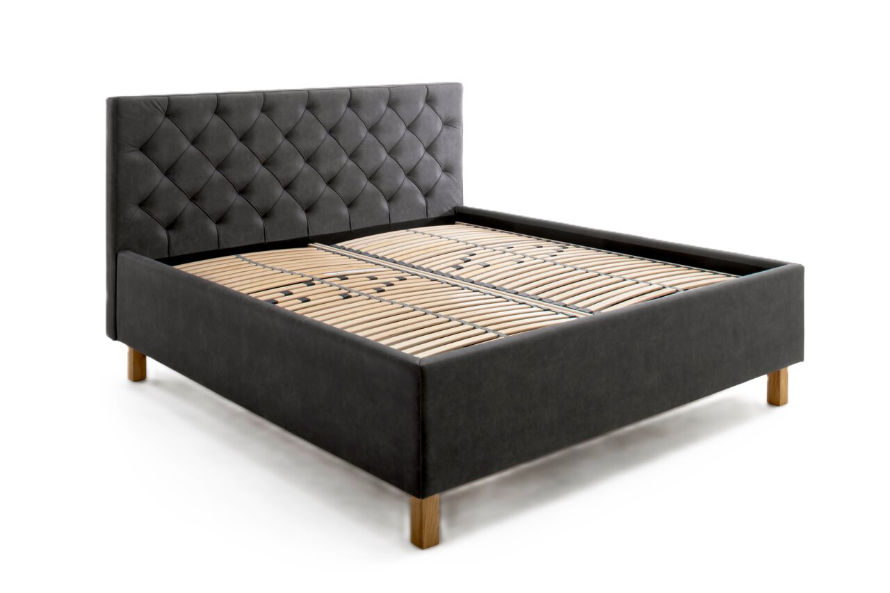 Zijaanzicht van een elegant gestoffeerd bed met een donkergrijs, doorgestikt hoofdeinde en houten poten.