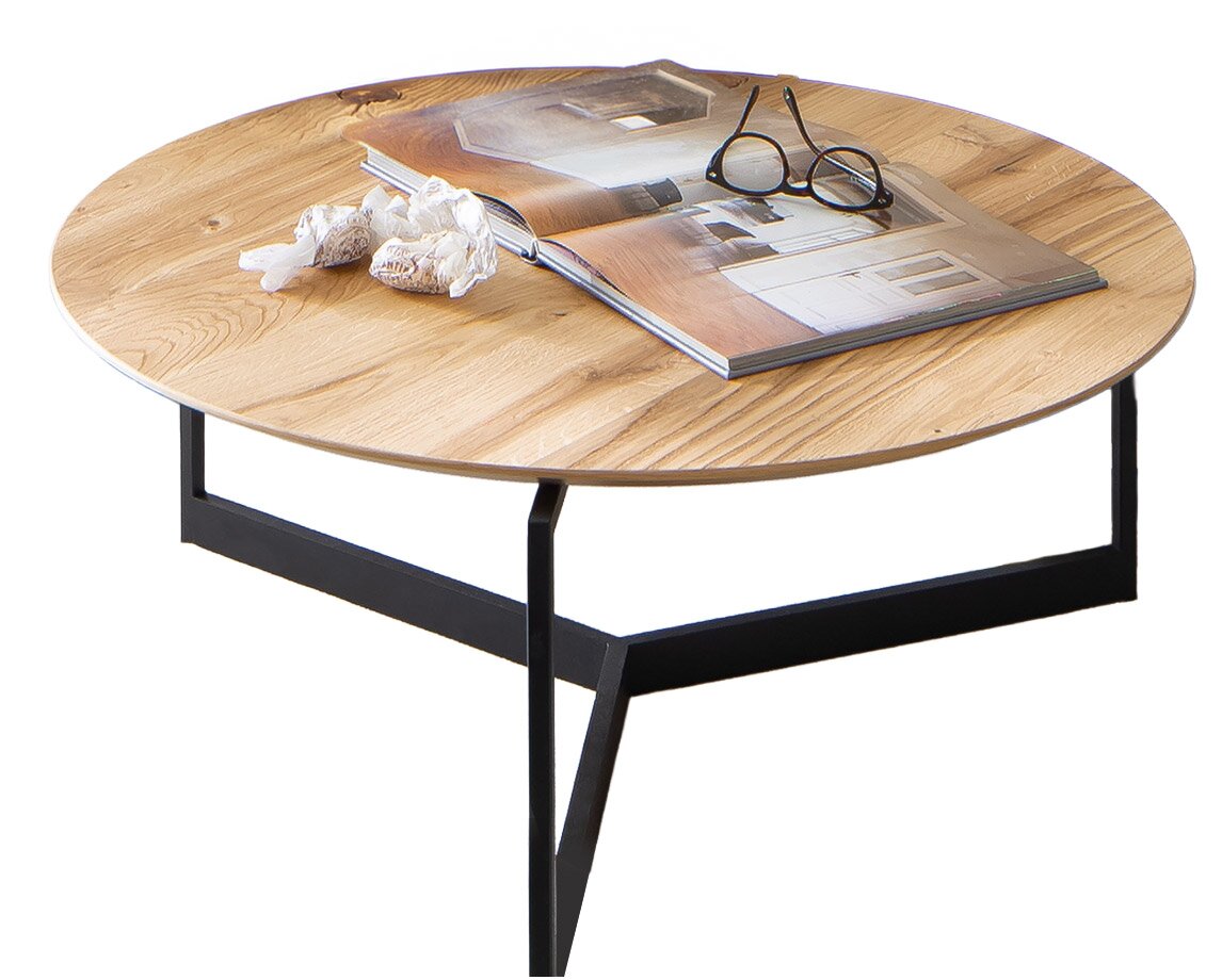 Ronde salontafel met licht houten blad en zwart metalen onderstel, gefotografeerd schuin van boven; op het blad liggen een open boek en een bril.