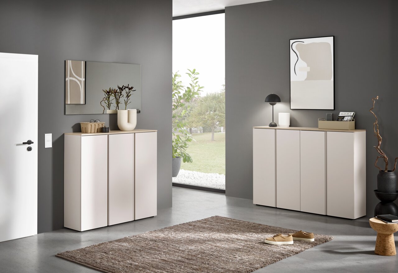 Voleo XXL-Schuhschrank MILTON Modernes Sideboard/Schuhschrank in Weiß mit Holzoptik-Deckplatte und drei Türen in einem minimalistischen Flur, frontale Perspektive auf das Möbelstück.