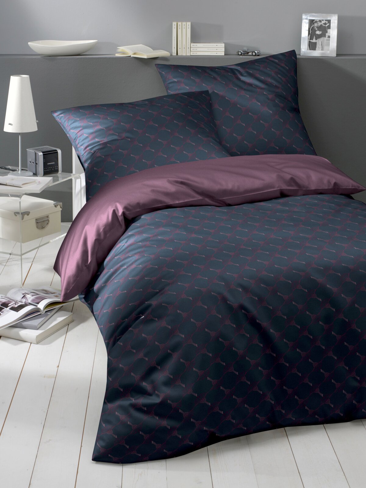 Bettwäsche-Set in dunklem Design mit geometrischem Muster, bestehend aus Kissen- und Bettdeckenbezug, auf einem Bett in einem modern eingerichteten Raum, seitliche Perspektive.