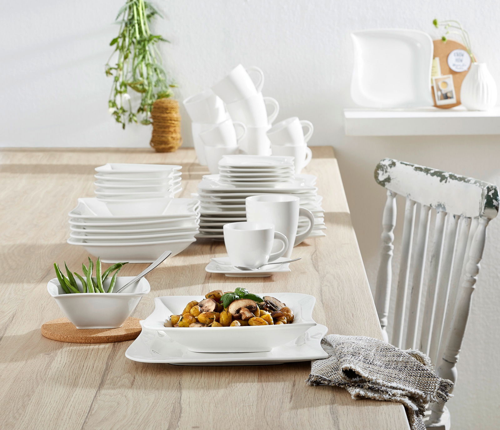 Kombiservice La Musica 42-tlg. auf einem Holztisch, mit elegantem, weißem Geschirr in moderner, quadratischer Form, aus der Perspektive von vorne aufgenommen.