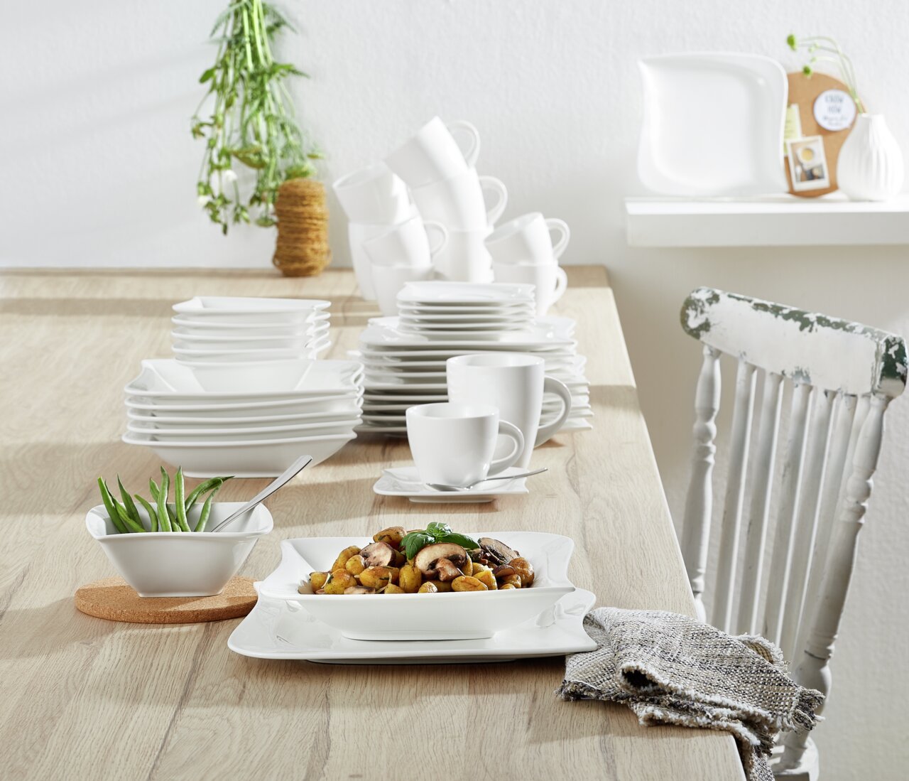 Kombiservice La Musica 42-tlg. auf einem Holztisch, mit elegantem, weißem Geschirr in moderner, quadratischer Form, aus der Perspektive von vorne aufgenommen.