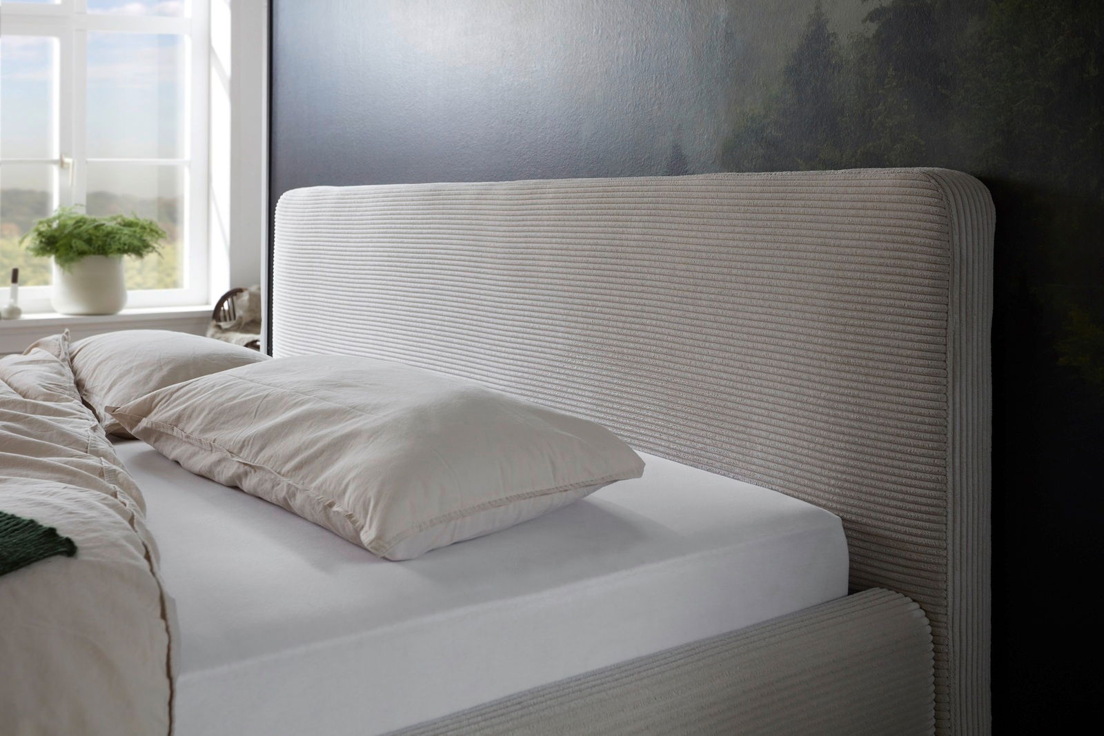 Seitliche Ansicht eines Polsterbettgestells mit gestreiftem Kopfteil in einem hellen Raum mit Fenster.