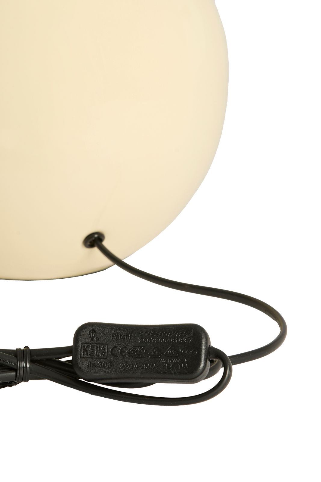 Nahaufnahme eines cremefarbenen Lampenfußes mit schwarzem Kabel und Schalter, von der Seite betrachtet.