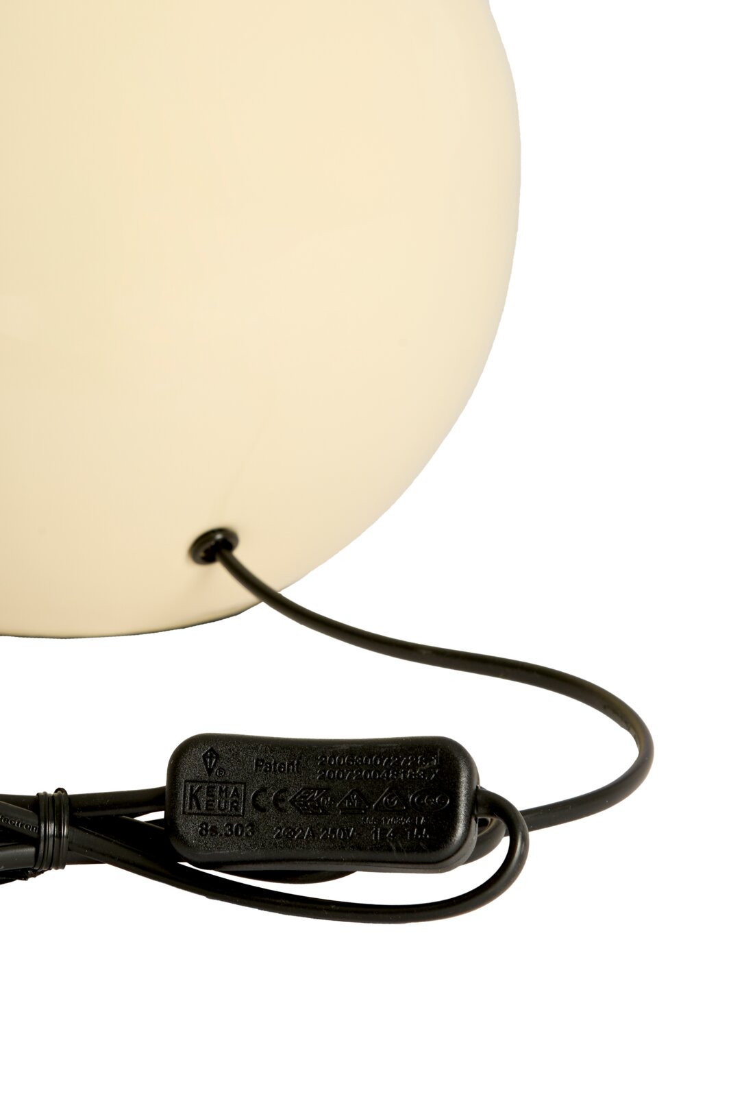 Close-up van een crèmekleurige lampvoet met een zwarte kabel en schakelaar, gezien vanaf de zijkant.