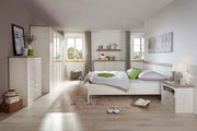 Helles Schlafzimmer mit einem 5-türigen Drehtürenschrank, Bett und Kommode in Holzoptik, seitliche Perspektive.
