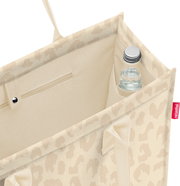 Blick von oben in eine beige gemusterte Einkaufstasche mit Innenfach und kleiner Flasche in der Ecke, Seitenansicht schräg von oben.