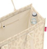 Blick von oben in eine beige gemusterte Einkaufstasche mit Innenfach und kleiner Flasche in der Ecke, Seitenansicht schräg von oben.
