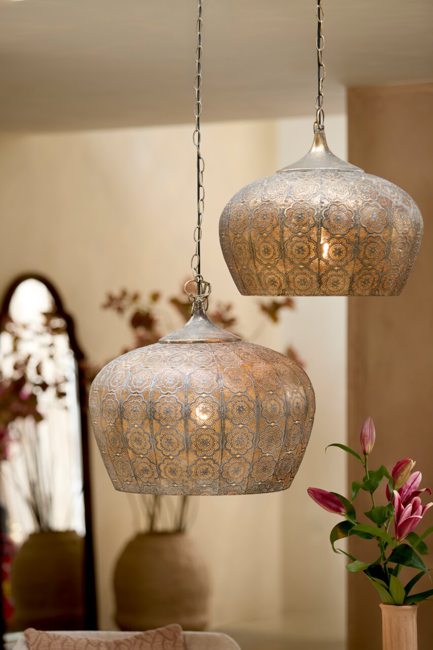 Twee oosterse hanglampen van metaal met een filigraanpatroon, gezien vanaf de zijkant, in een stijlvol ingerichte ruimte.
