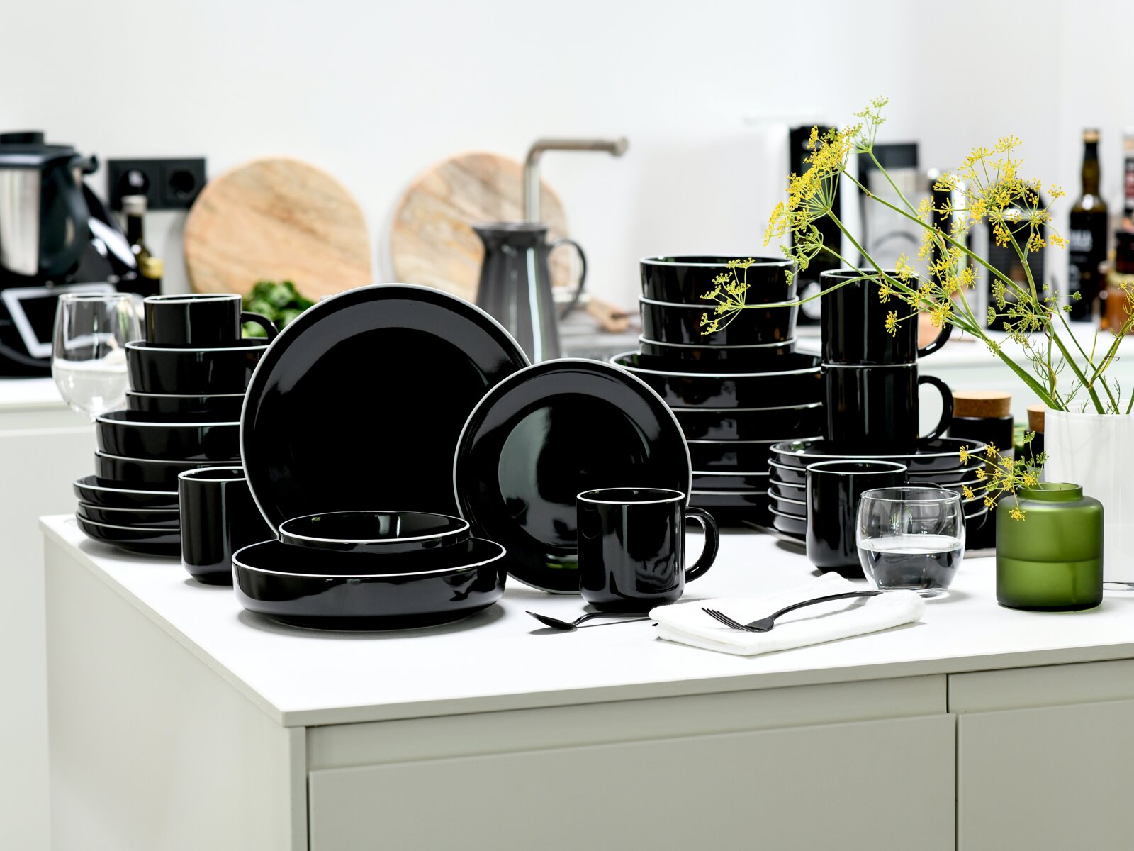 creaTable Kombiservice 30-tlg NORDIC GOURMET Schwarzes, glänzendes Geschirrset mit Tellern, Schalen und Bechern auf weißer Kücheninsel, perspektivisch in leichter Seitenansicht von vorn fotografiert.