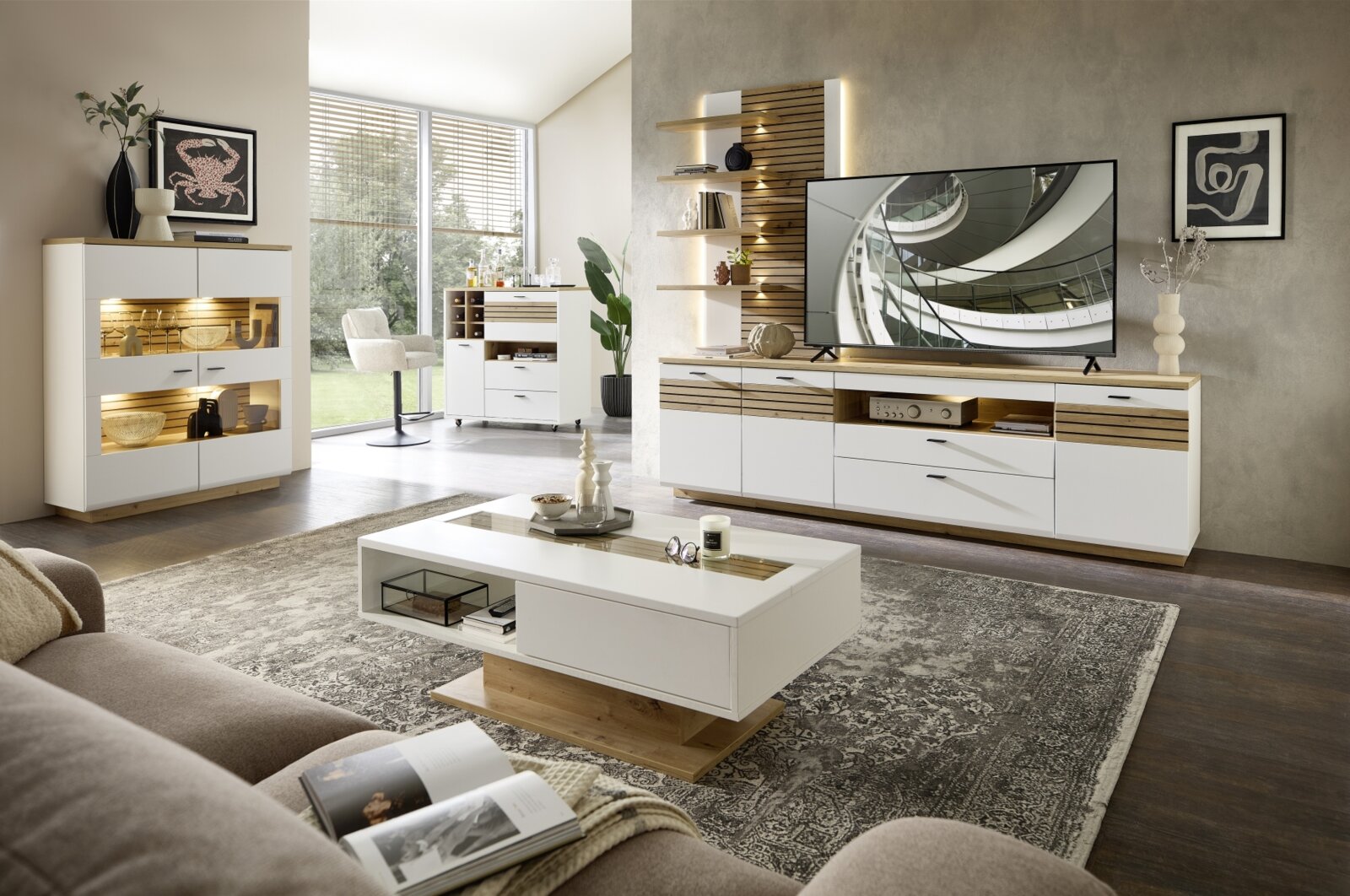 Moderne woonkamerwandcombinatie in wit en houtlook, met tv-kast, planken en sfeerverlichting, gezien vanuit een gezellige woonkamer.
