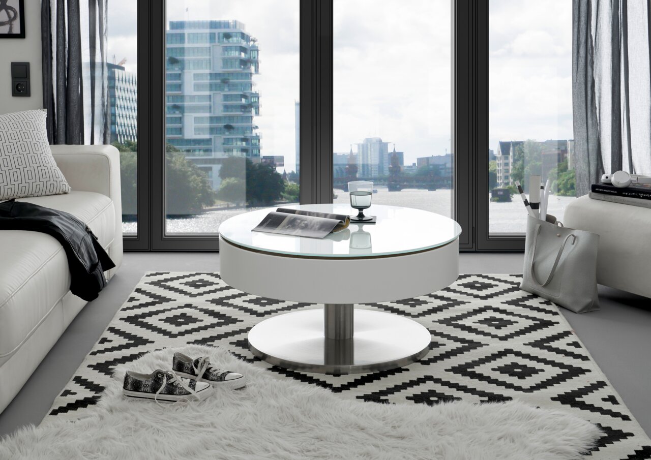 Moderner runder Couchtisch mit Glasplatte in einem stilvollen Wohnzimmer mit Blick auf die Stadt durch große Fenster, von vorne betrachtet.