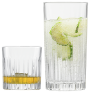 Zwei Whiskygläser im Set, eines mit Whisky und Eis, das andere mit einem sprudelnden Getränk und Limettenscheiben, aus seitlicher Perspektive fotografiert.