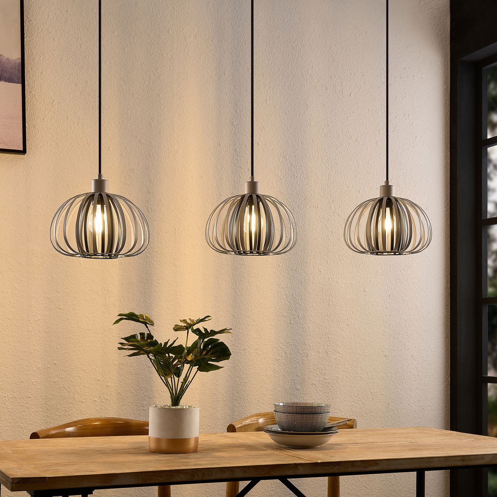 Novel Hängeleuchte Drei moderne Hängeleuchten mit Metallkäfig-Design über einem Esstisch, seitliche Perspektive.