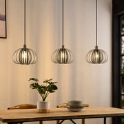 Drei moderne Hängeleuchten mit Metallkäfig-Design über einem Esstisch, seitliche Perspektive.
