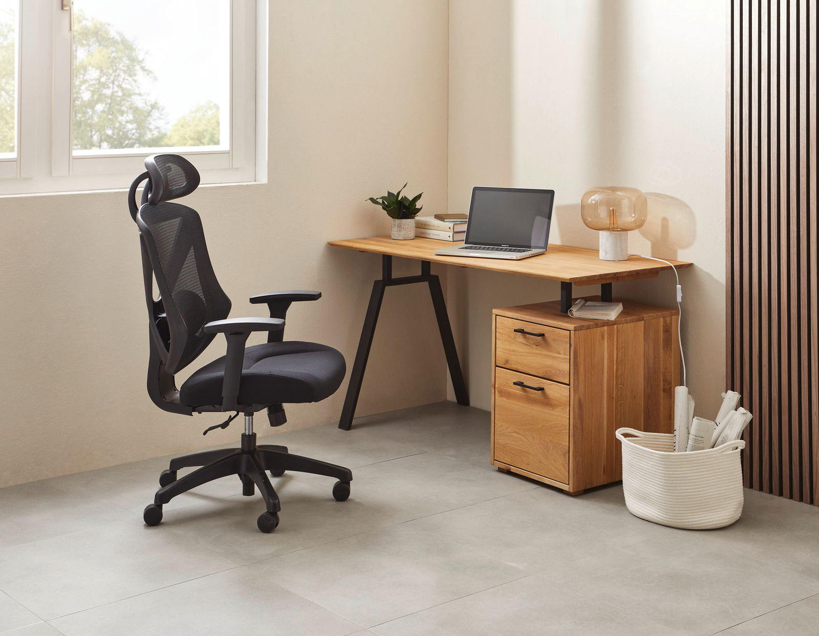 Moderner Schreibtisch mit Holzoberfläche und schwarzem Metallgestell, seitlich mit Schubladen, in einem hellen Raum mit ergonomischem Bürostuhl.