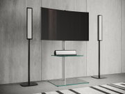 Modernes TV-Heimkino-Setup mit großem Flachbildschirm auf silbernem Standfuß mit Glasboden und Glasablage sowie zwei schlanken Standlautsprechern links und rechts vor Betonwand, Frontalansicht