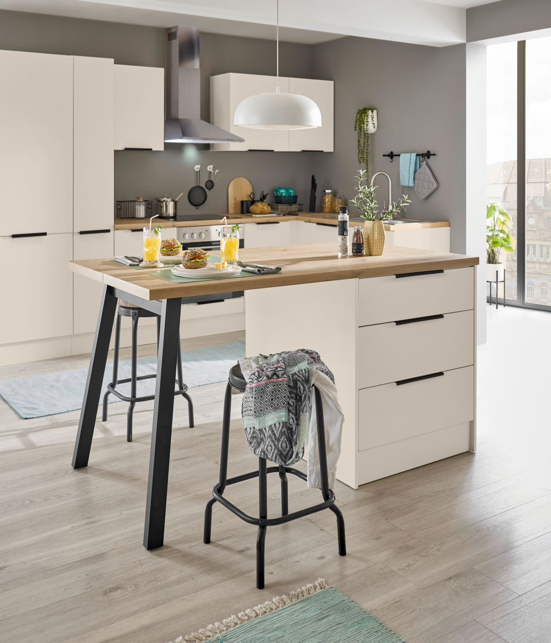 Moderne, helle Küche mit Kücheninsel in Weiß und Holzoptik, schwarzen Griffen und Barhockern, aufgenommen aus leicht erhöhter Front-/Schrägperspektive.