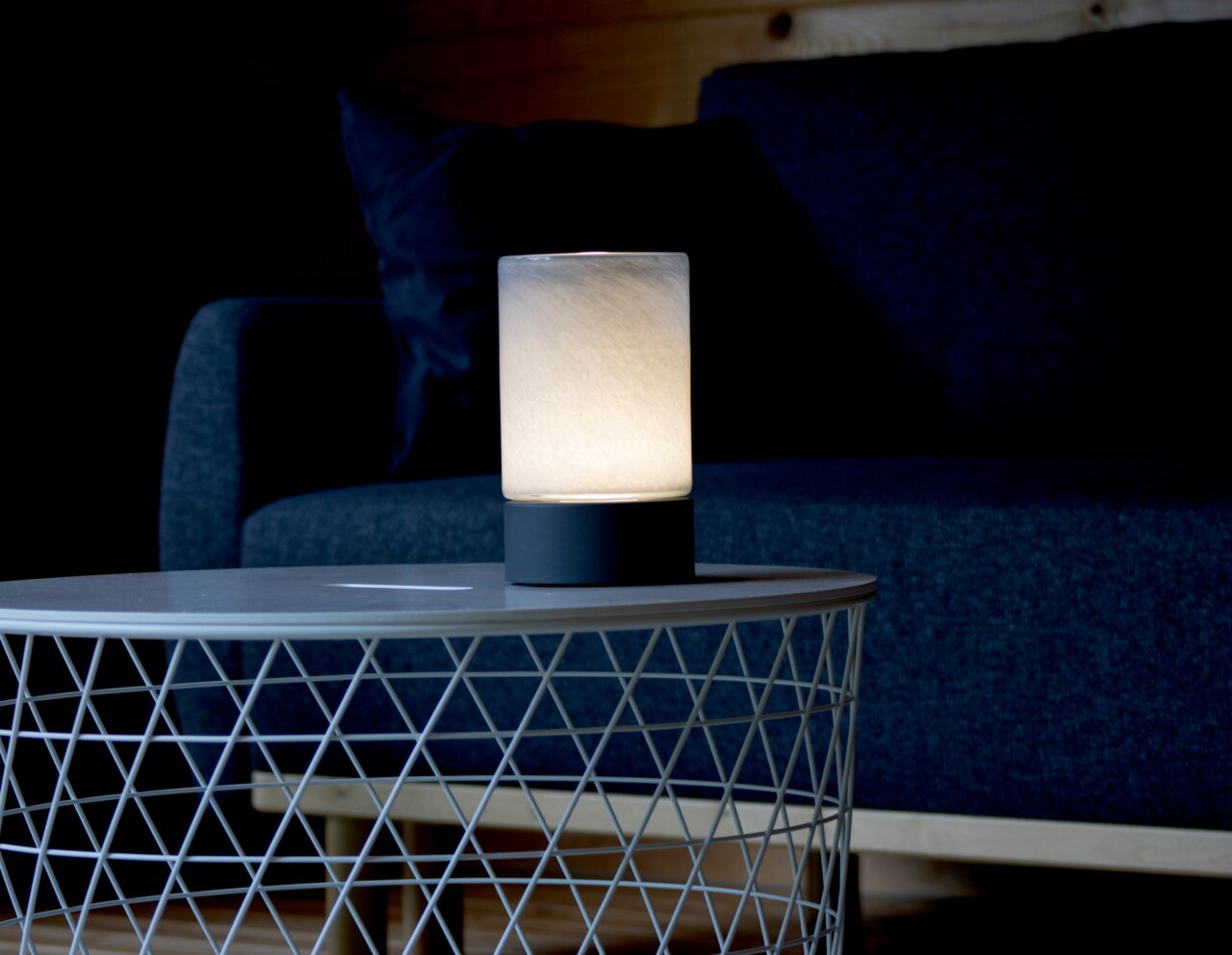 Akku-Windlicht auf einem Tisch vor einem Sofa, seitliche Perspektive