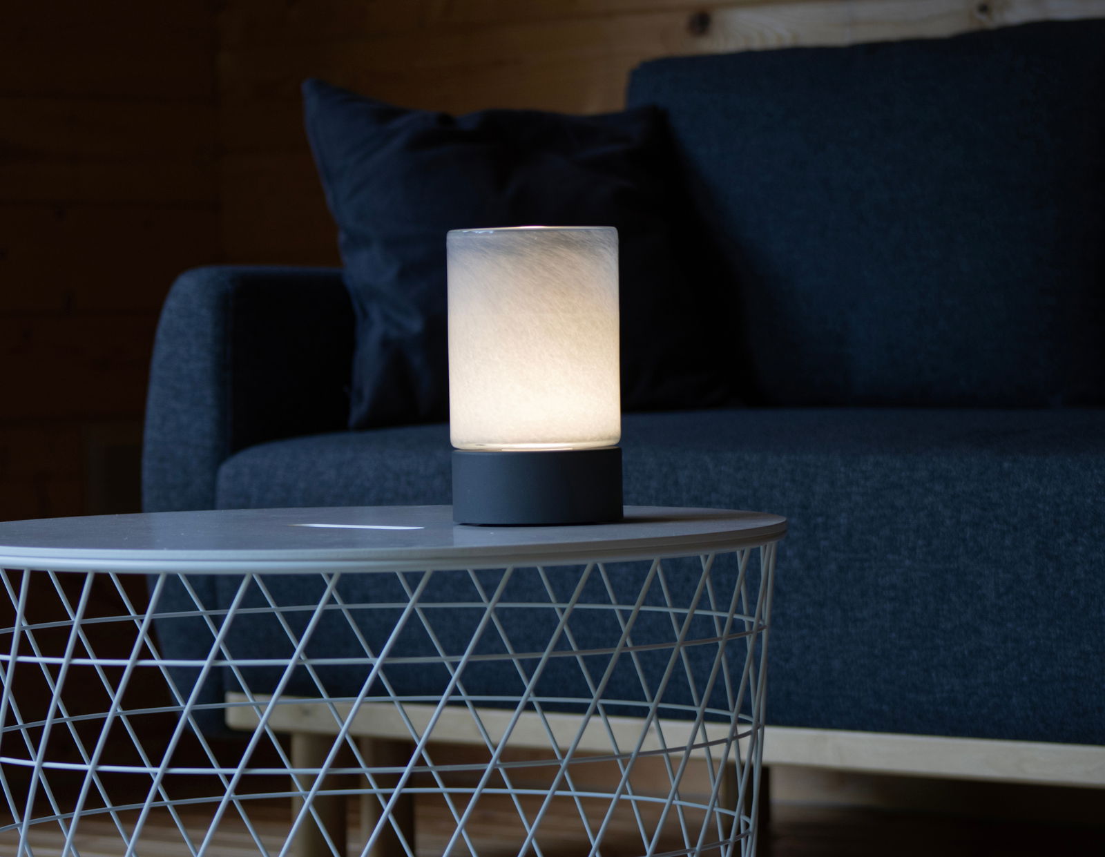 Akku-Windlicht auf einem Tisch vor einem Sofa, seitliche Perspektive