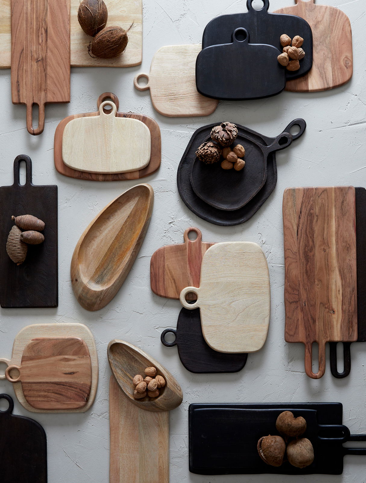 Verschiedene Schneidebretter aus Holz in unterschiedlichen Formen und Farben, von oben betrachtet, dekoriert mit Nüssen.