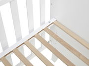 Nahaufnahme eines Babybetts mit weißen Gitterstäben und einem Lattenrost aus hellem Holz, von oben betrachtet.
