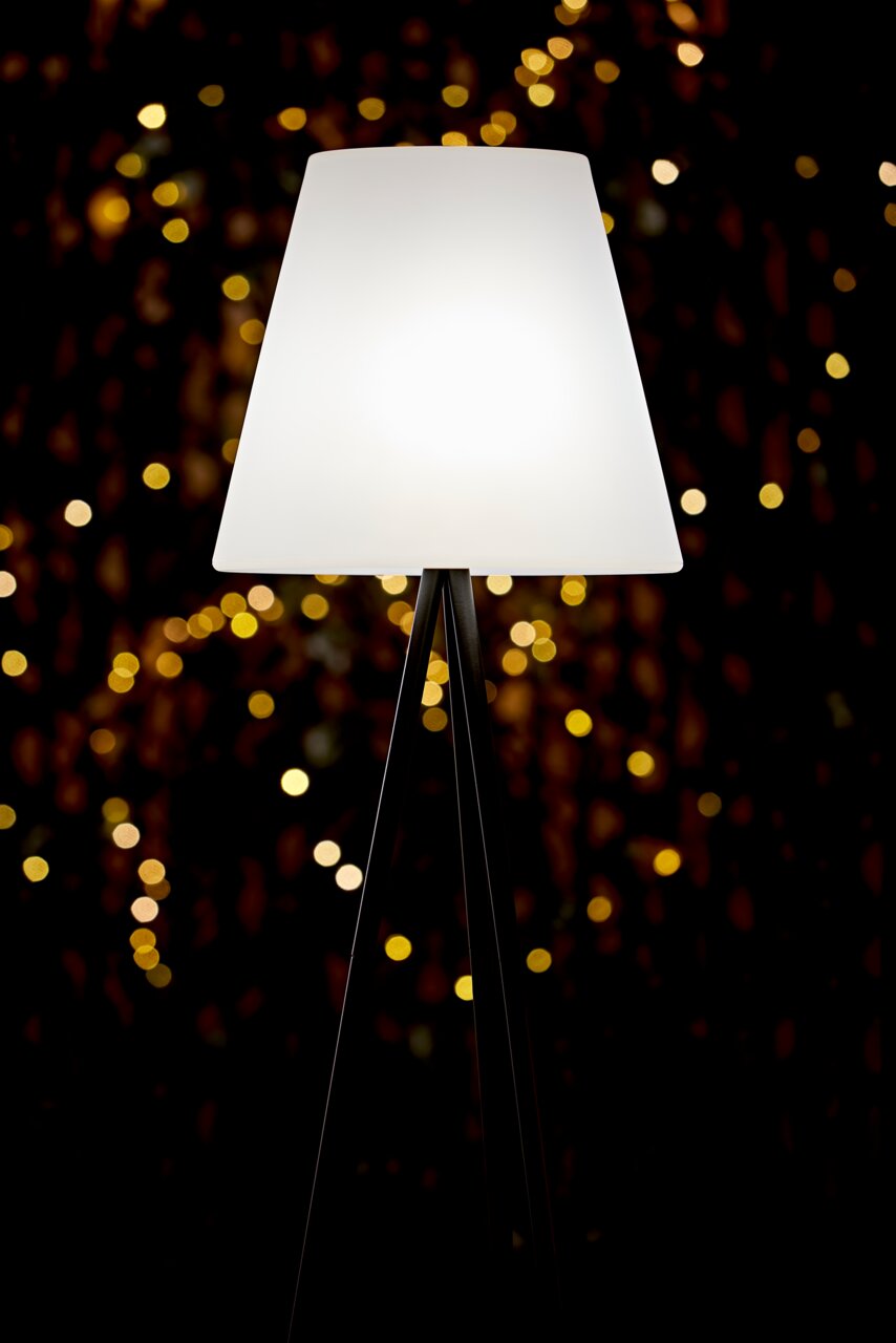 Kynast Exclusive Solar Standleuchte Solar Standleuchte mit dreibeinigem Stativ und weißem Lampenschirm, beleuchtet in einer stimmungsvollen Umgebung, seitliche Perspektive