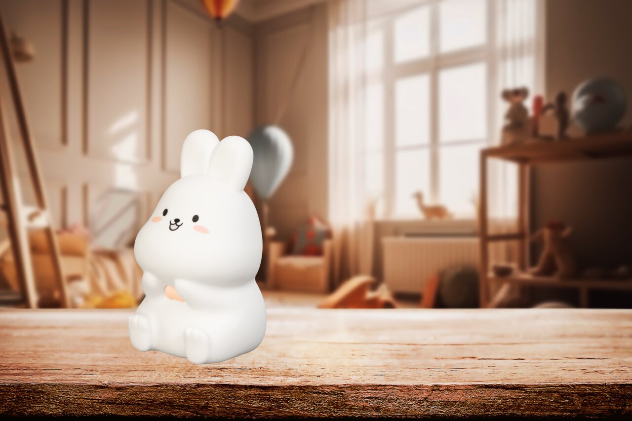 Niedliches Akku-Nachtlicht in Form eines sitzenden Hasen, frontal fotografiert, auf einem Holztisch in einem gemütlichen Kinderzimmer.