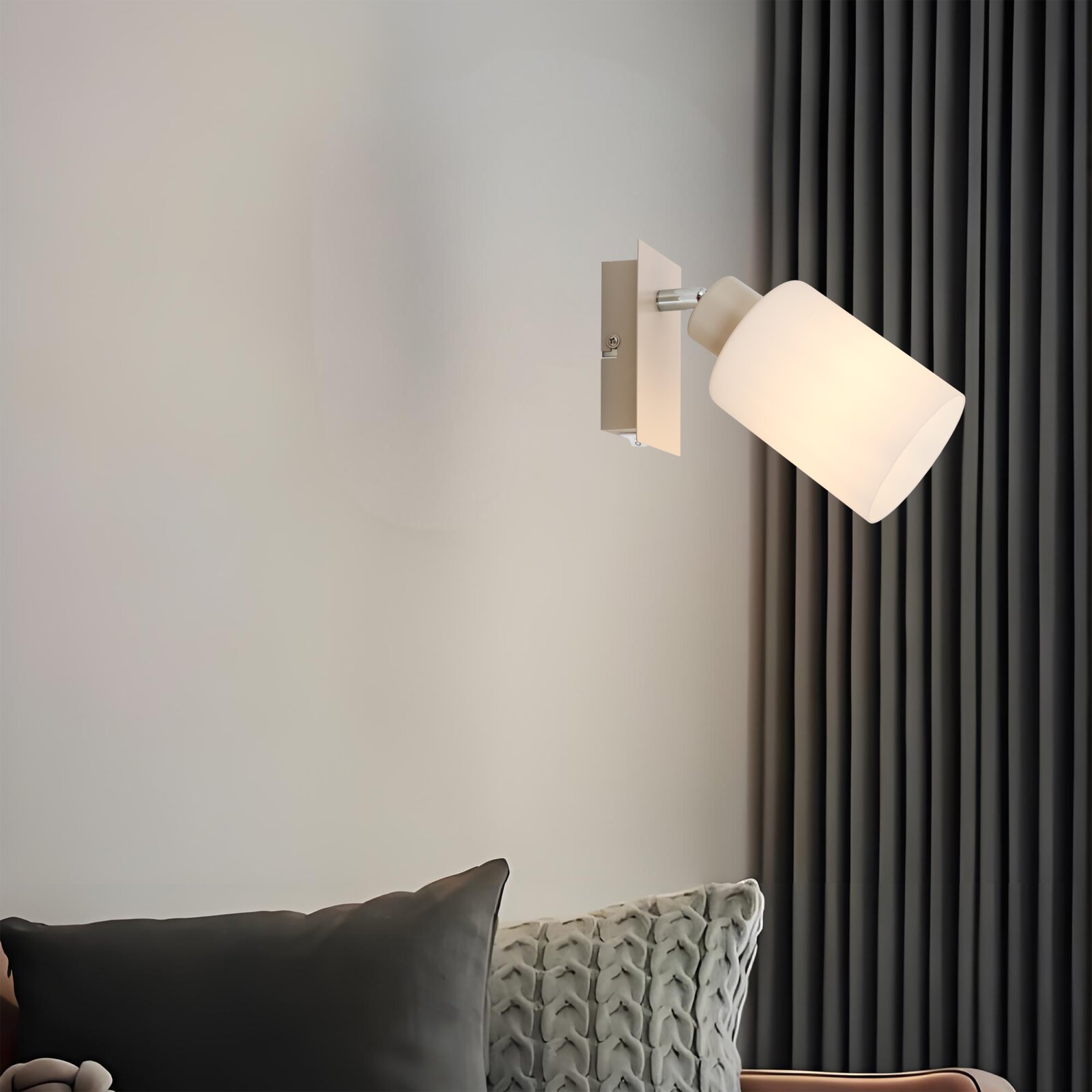 Moderne weiße Wandleuchte mit zylindrischem Lampenschirm und eckiger Wandhalterung, eingeschaltet an heller Wand neben dunklen Vorhängen, seitliche Perspektive