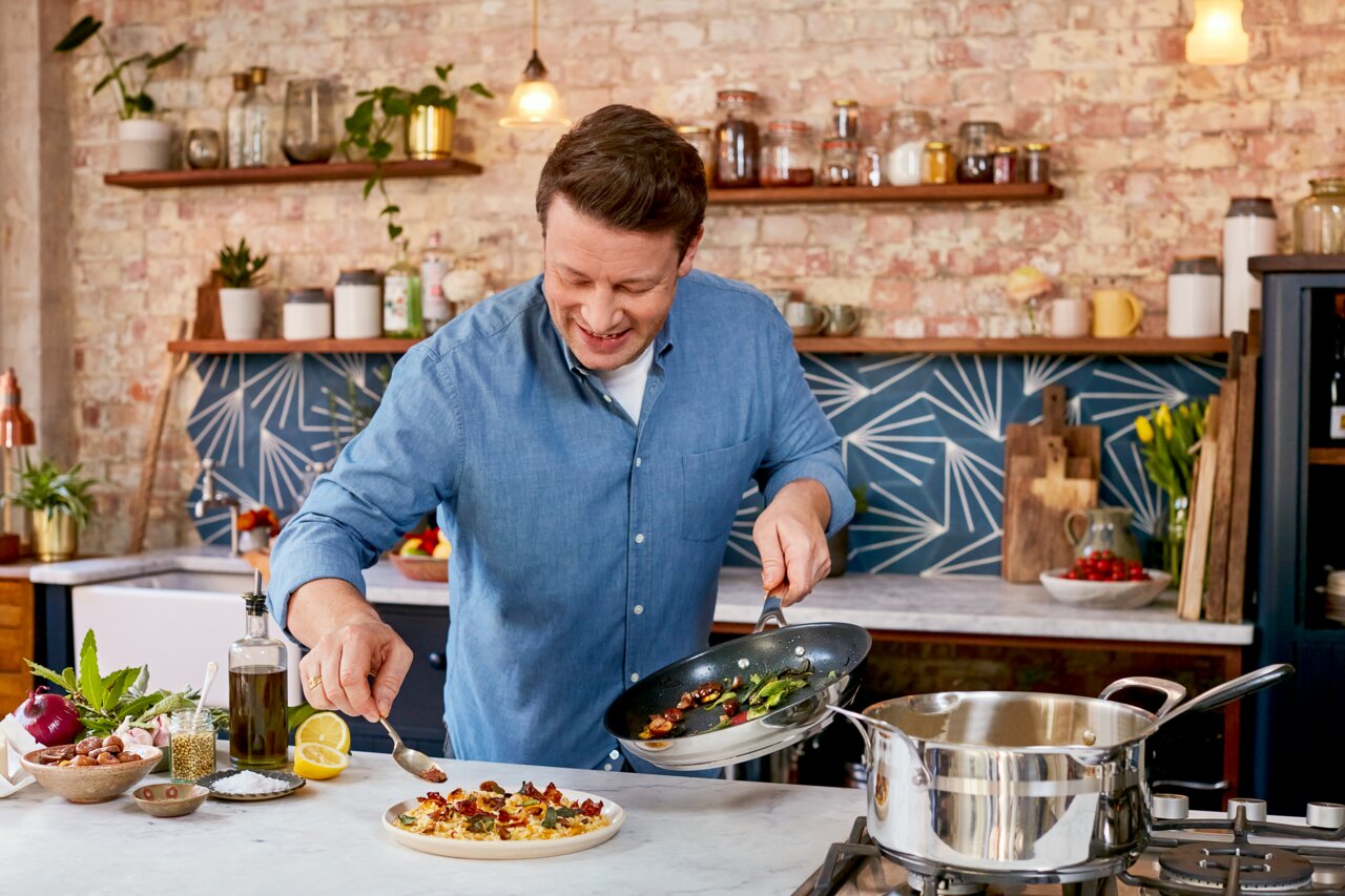 Tefal Bratpfanne 28 cm Jamie Oliver Smart Koch in einer modernen Küche, der eine Bratpfanne hält und ein Gericht anrichtet. Die Perspektive zeigt die Pfanne von oben.
