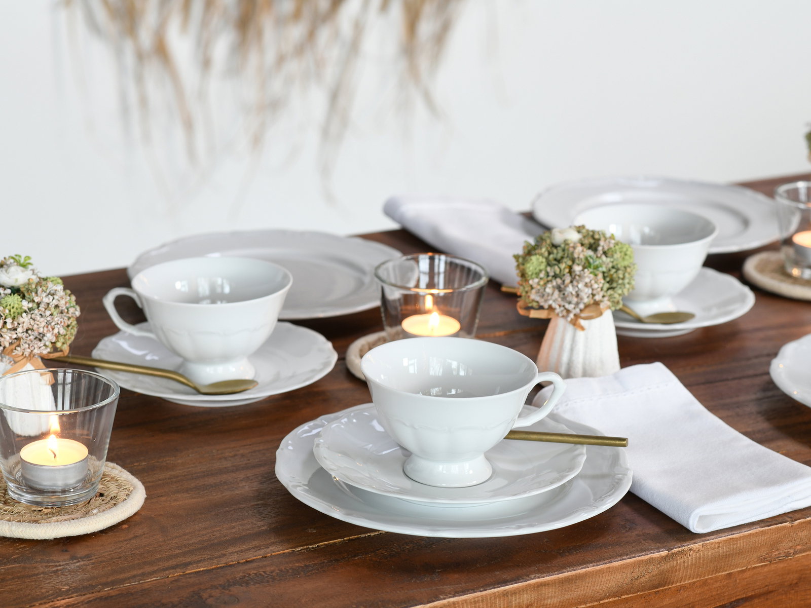 Elegantes Kaffeeservice 18-tlg auf einem gedeckten Tisch, seitliche Perspektive mit Kerzen und Blumenarrangement.