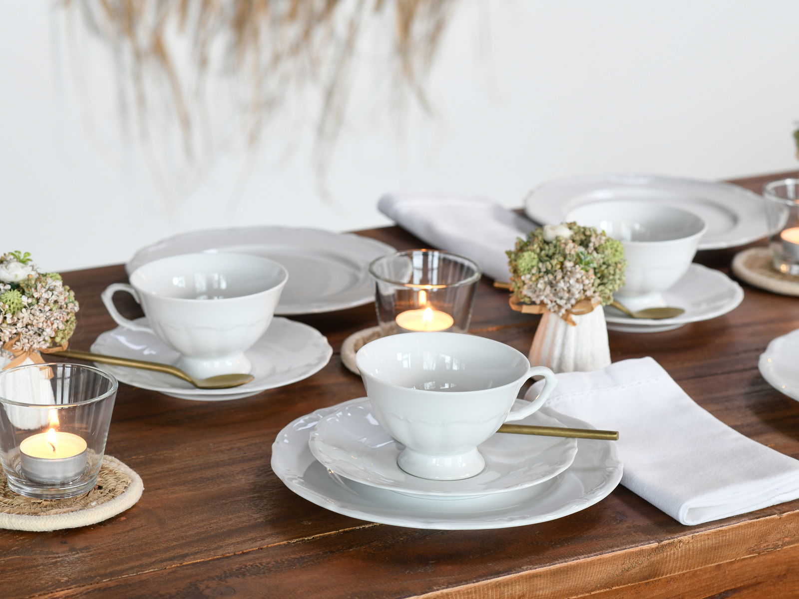 Elegantes Kaffeeservice 18-tlg auf einem gedeckten Tisch, seitliche Perspektive mit Kerzen und Blumenarrangement.