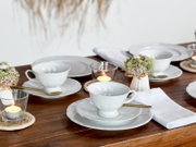 Elegantes Kaffeeservice 18-tlg auf einem gedeckten Tisch, seitliche Perspektive mit Kerzen und Blumenarrangement.