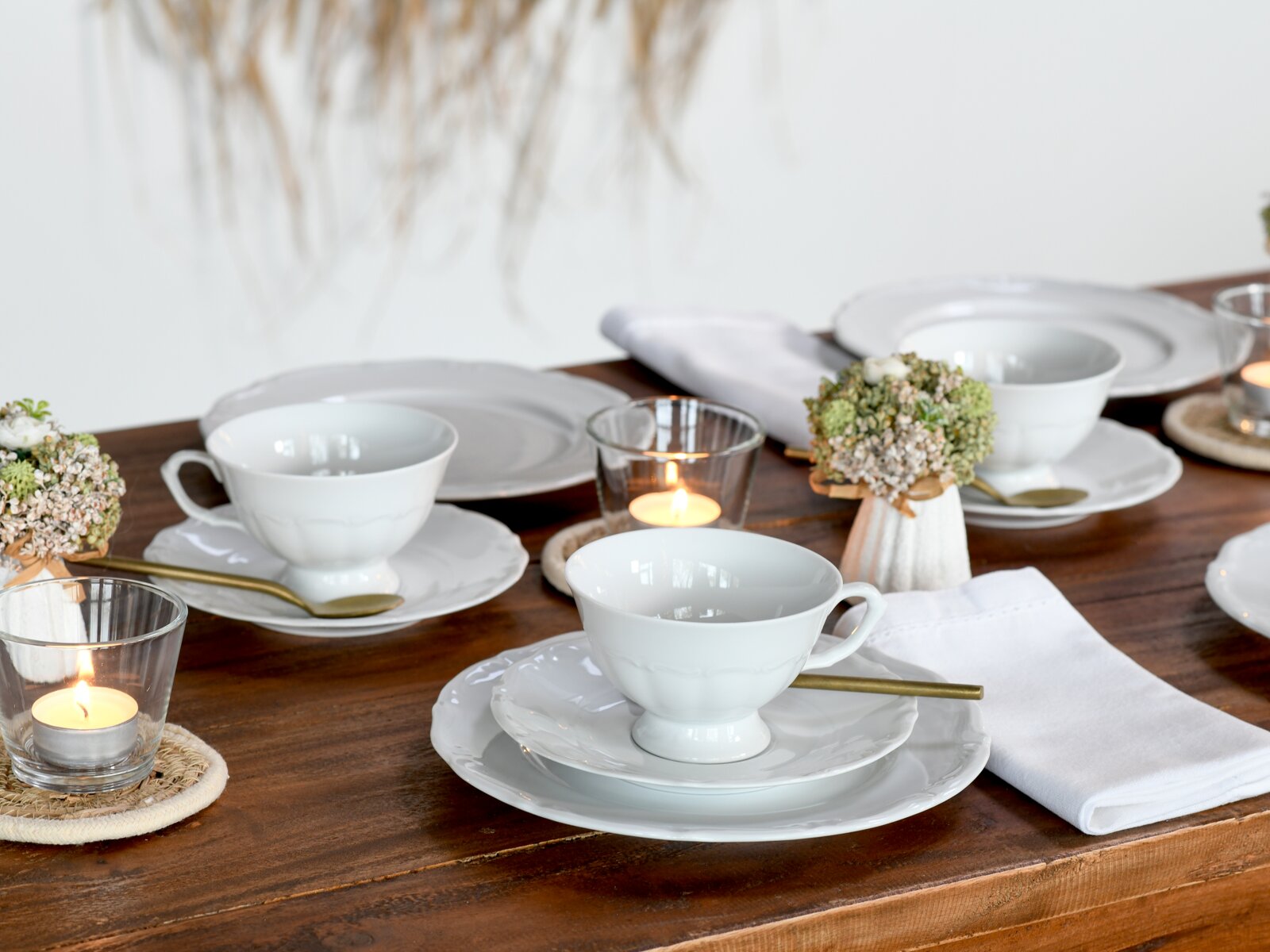 Elegantes Kaffeeservice 18-tlg auf einem gedeckten Tisch, seitliche Perspektive mit Kerzen und Blumenarrangement.